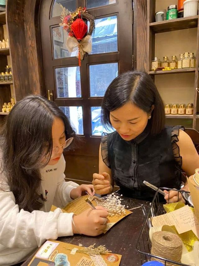 Hai mẹ con cùng ngồi làm thiệp hoa khô trong một tiệm thủ công.